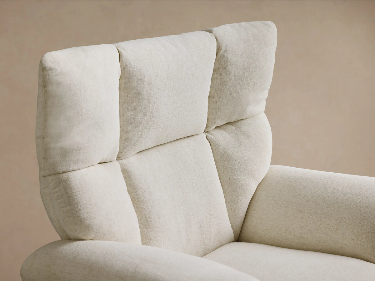 Side-rear view of the cream Deacon Swivel Recliner in textured fabric, with a padded back, vertical seams, and a gold swivel base.