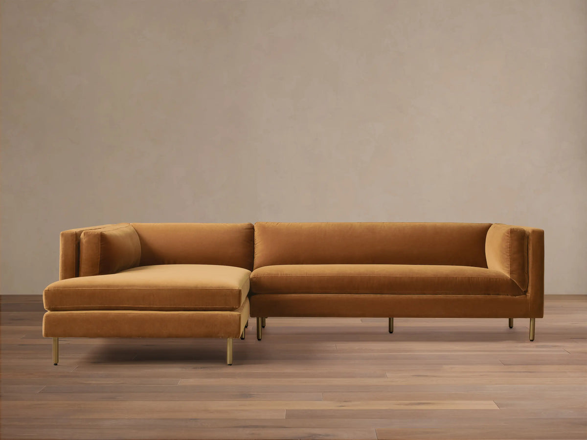 Front view of a mustard velvet Malta Two-Piece Chaise Sectional with the chaise on the left and recessed gold legs.