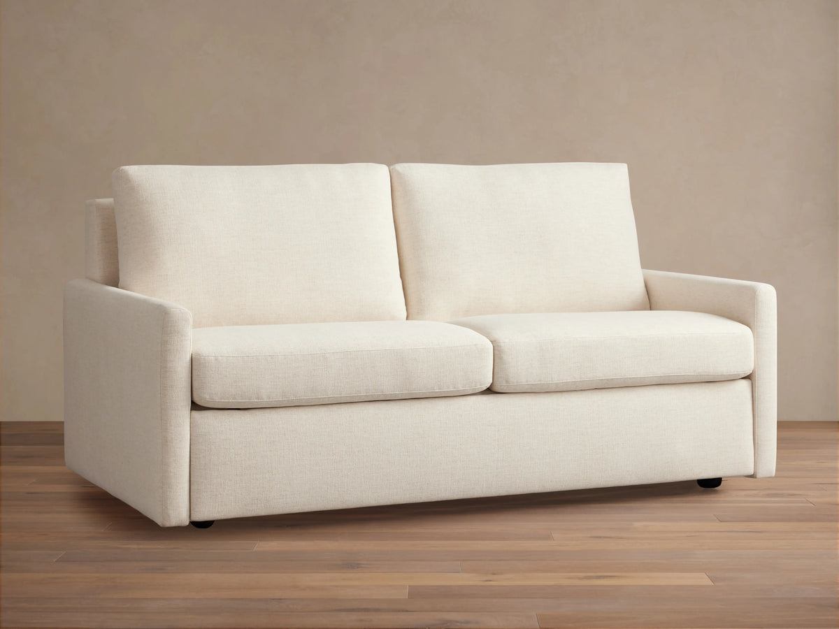 Kipton Luxury Sleeper Sofa in cream fabric, with clean lines, two cushions, and a sleek design, placed on wooden floor.