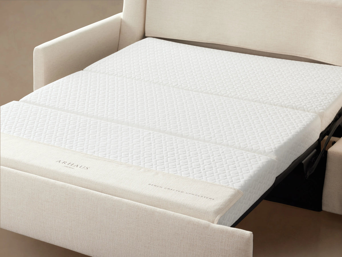 Kipton Luxury Sleeper Sofa in beige fabric, with plush cushions and armrests, placed on a wooden floor against a neutral wall.