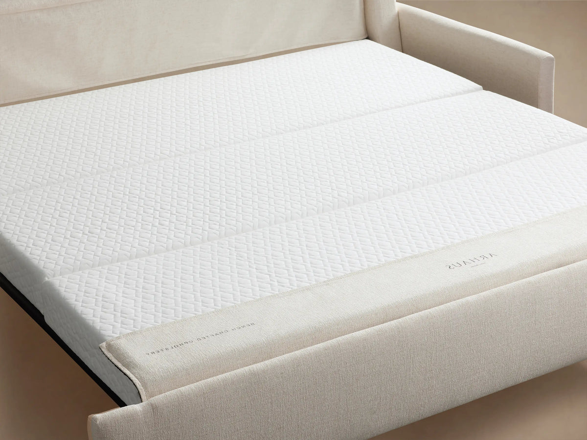 Kipton Slim Arm Luxury King Sleeper Sofa in Wiley Parchment, a light cream-colored sofa with slim arms, on a wooden floor.