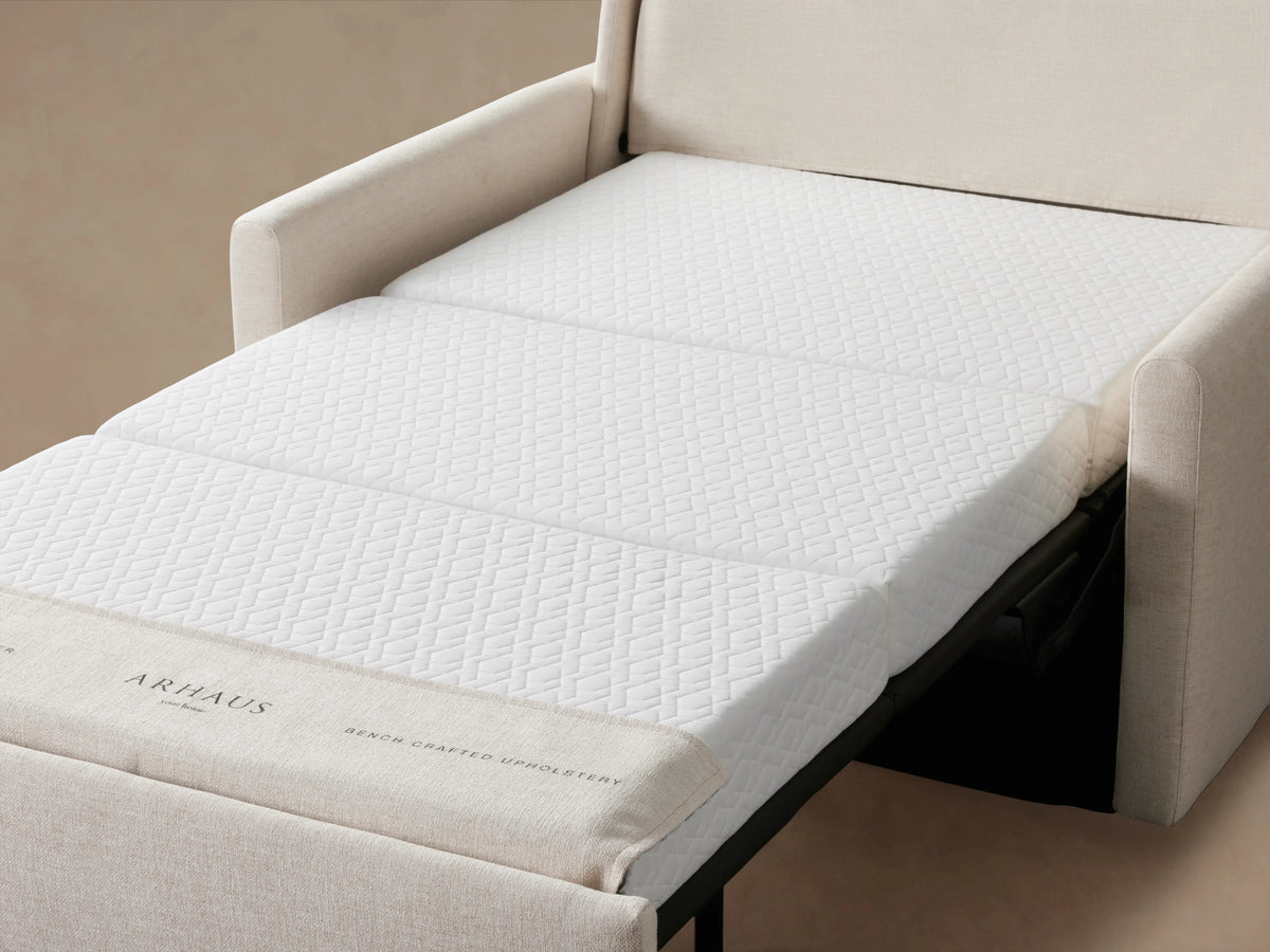 Kipton Slim Arm Luxury Twin Sleeper Chair in light beige fabric, featuring cushioned backrest, sleek armrests, on a wooden floor.