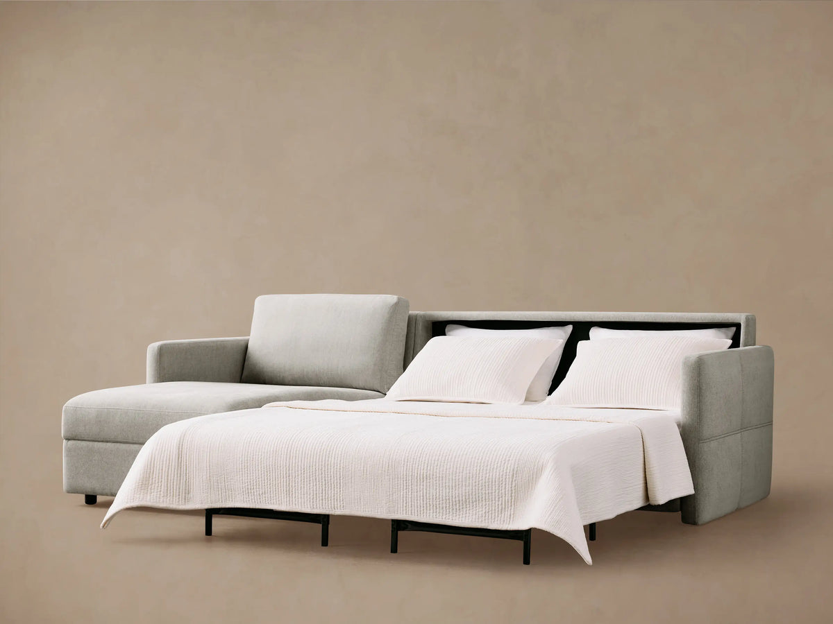 Reece Two-Piece Sleeper Chaise Sectional in light grey, partially open to reveal the white sleeper mattress & black frame.