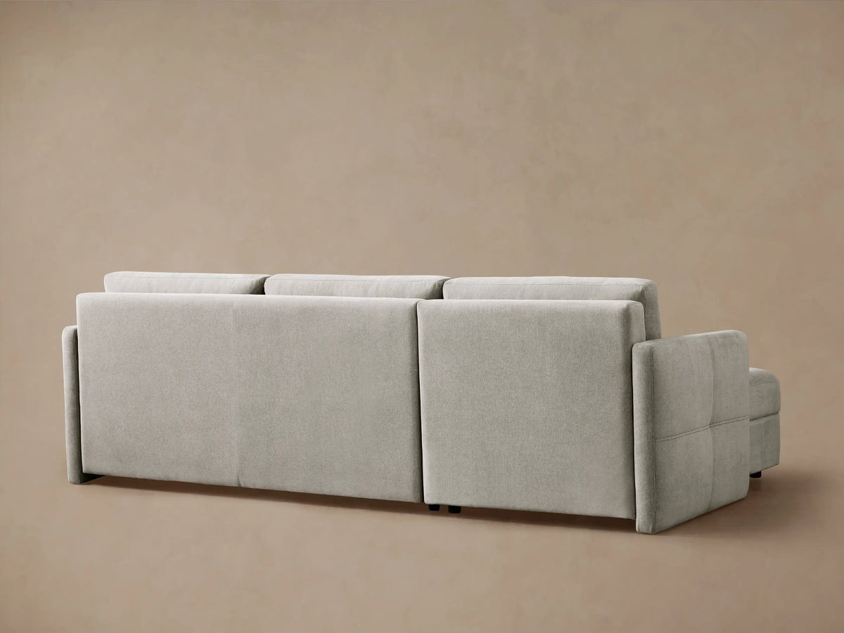 Reece Two-Piece Sleeper Chaise Sectional in light gray, with the sleeper extended as a bed, covered with white bedding, on a plain background.