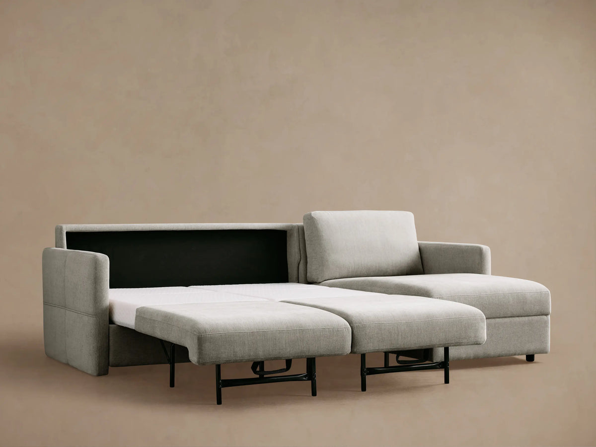 Light grey Reece Two-Piece Sleeper Chaise Sectional with white quilted foam mattress partially pulled out, showing armrest.