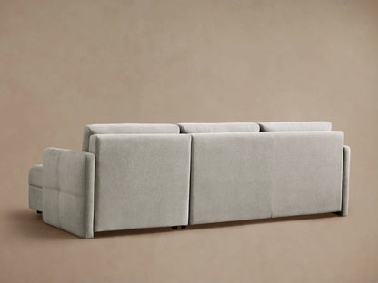 Light gray Reece Two-Piece Sleeper Chaise Sectional, left side converted to bed with white quilt & pillows, chaise right.