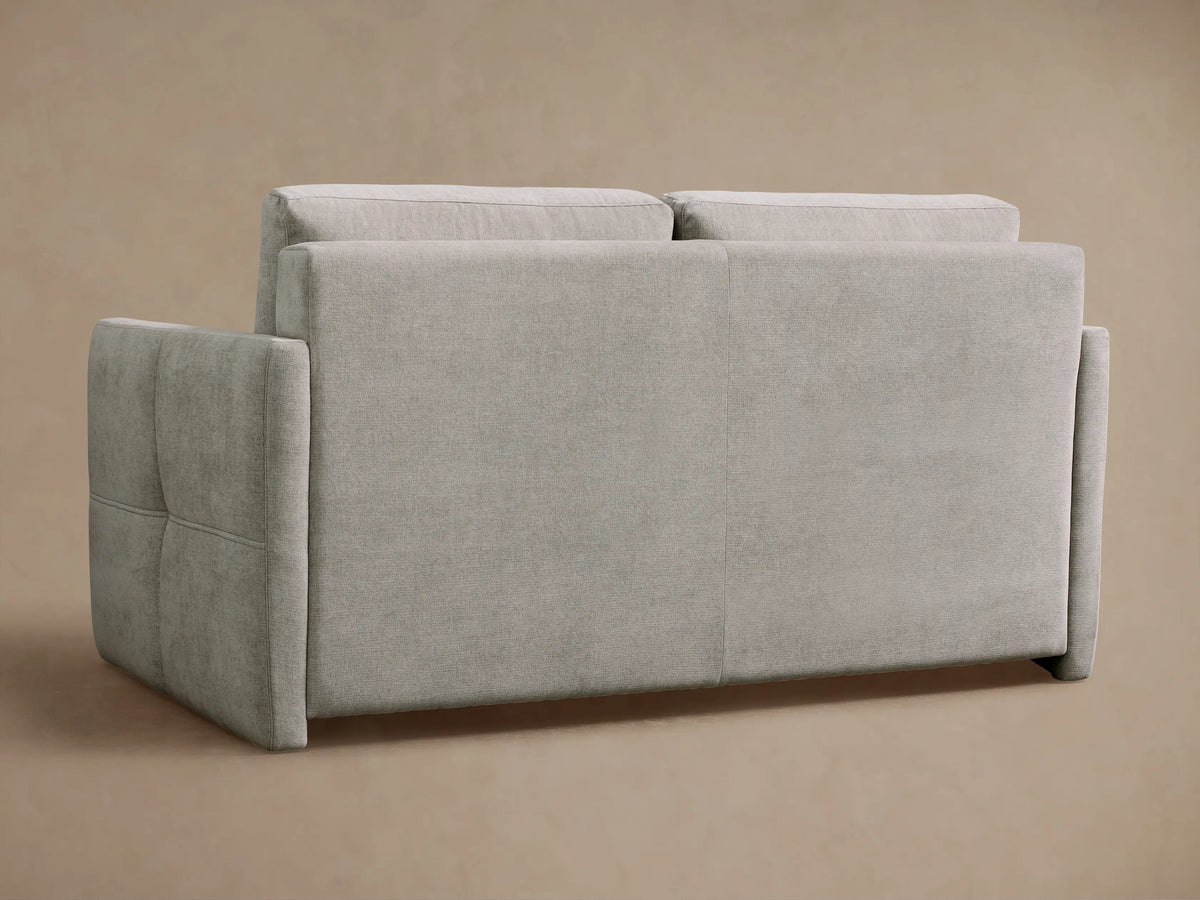 Close-up of Reece Sleeper Sofa in light gray fabric, with its backrest cushion lifted to reveal a white quilted mattress and black interior.