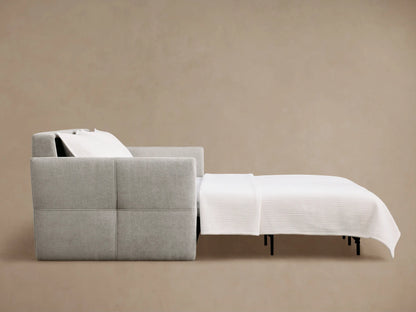 Reece Sleeper Sofa in light gray fabric, partially open to reveal a white mattress and extending upholstered footrest with black legs.