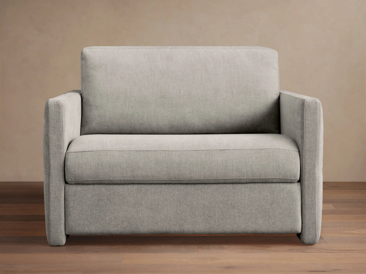 Reece Twin Sleeper Chair in light gray fabric, a modern upholstered armchair with square arms and clean lines, on a wooden floor.