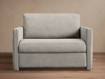 Reece Twin Sleeper Chair in light gray fabric, a modern upholstered armchair with square arms and clean lines, on a wooden floor.