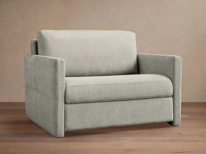 Reece Twin Sleeper Chair in light gray fabric, a modern upholstered armchair with square arms and clean lines, on a wooden floor.
