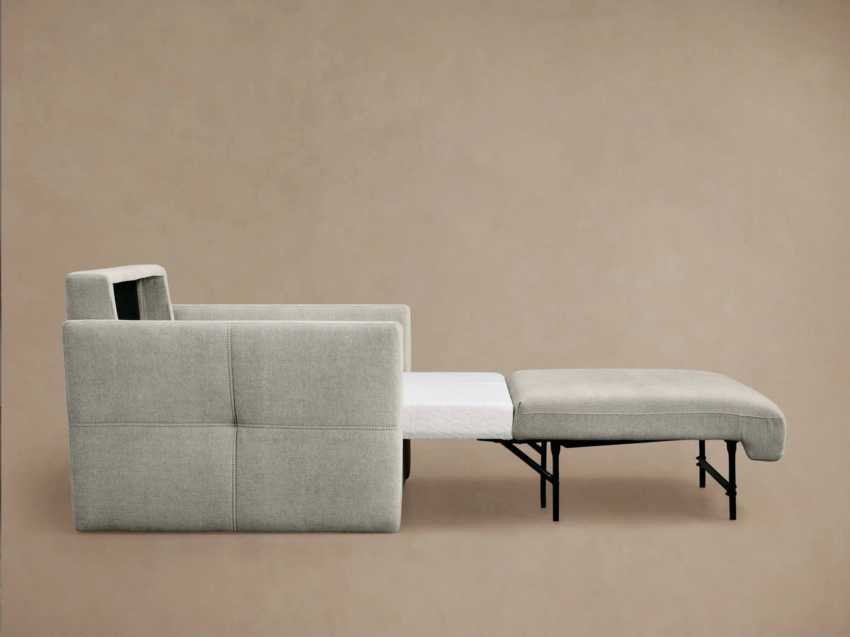 Angled back view of a light grey Reece Twin Sleeper Chair, showing its upholstered body, loose back cushion, and stitched armrest.