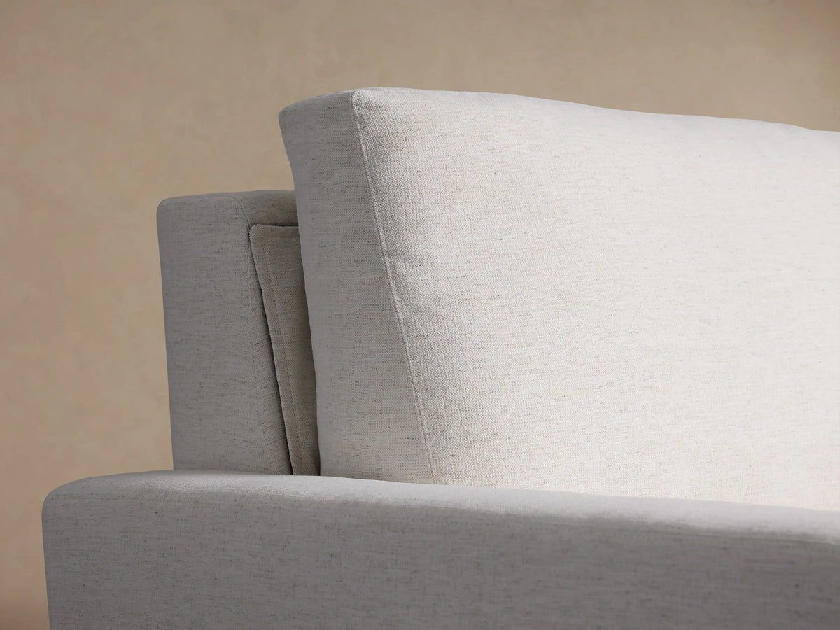White Remington Luxury Sleeper Sofa, a modern upholstered two-seater with wide arms and dark base, on a wooden floor.