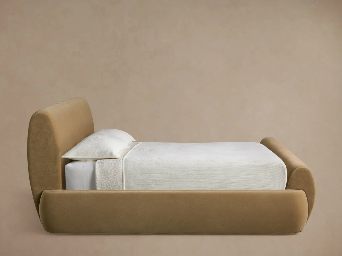 Close-up of Wynn Bed's rounded, upholstered headboard in tan/beige, showing detailed double stitching along the curve.