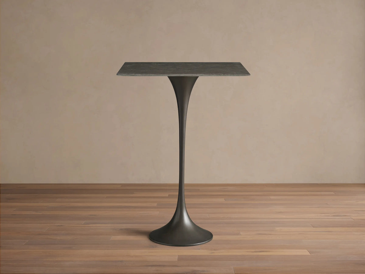 Front view of the Saint Germain Square Bar Table, featuring a dark gray square stone top and a flared steel base.