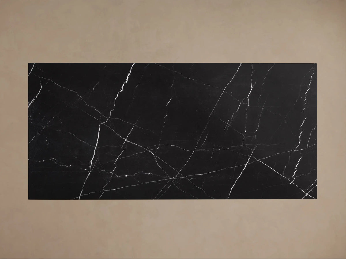 Front view of a black marble dining table with prominent white veining, featuring a rectangular top and a solid trapezoidal base.