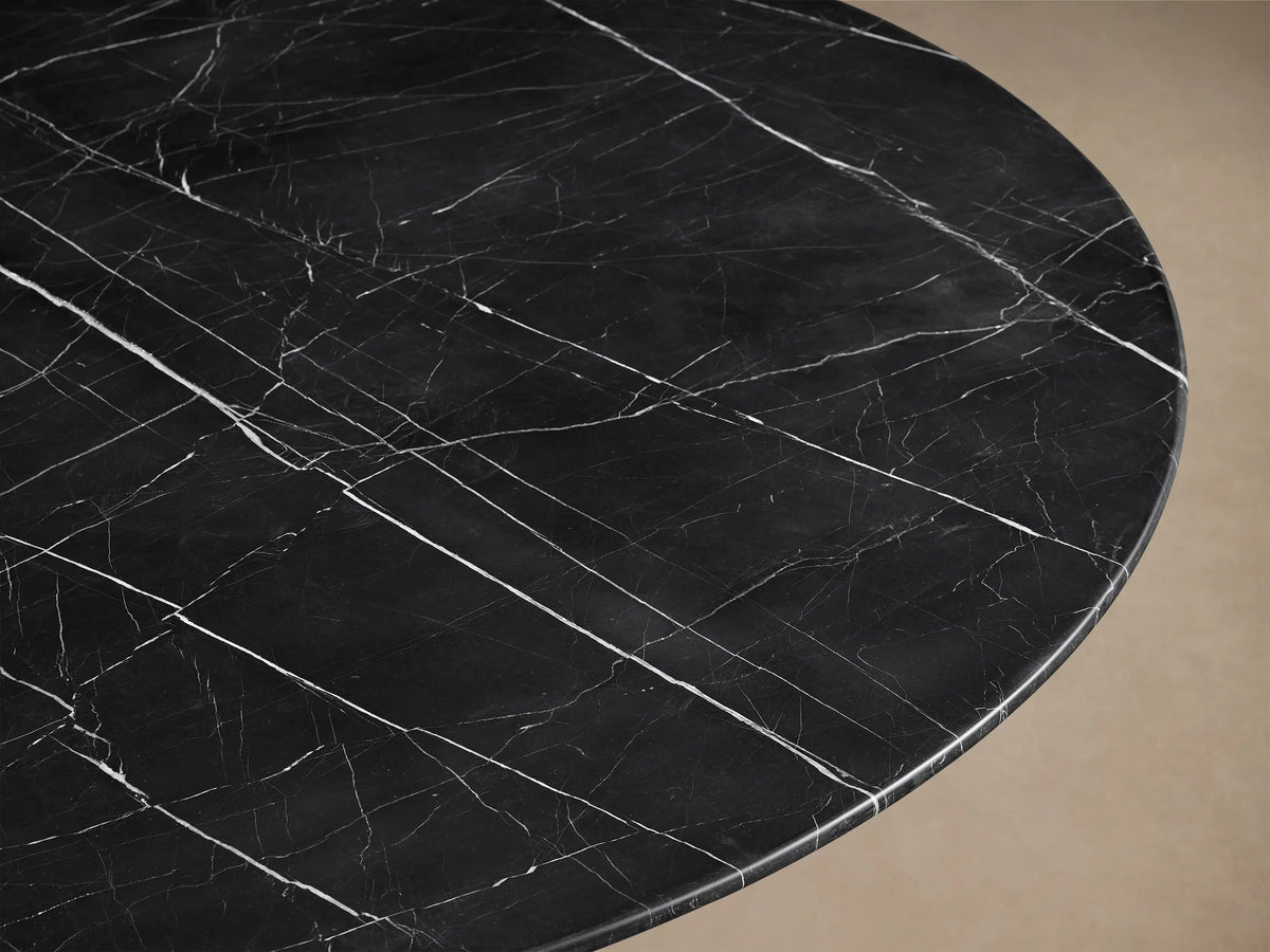Front view of the black Saint Germain Round Stone Dining Table with Toulouse Base, featuring a dark stone top with white veining and a tapered black wood base.