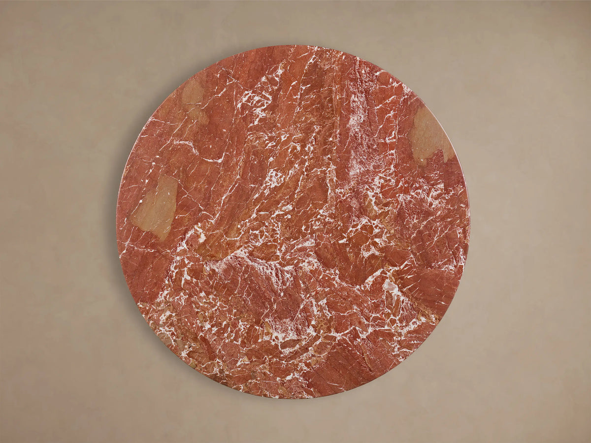 Front view of the Saint Germain Round Stone Dining Table with Toulouse Base, showing a round red stone top with white veining on a black tapered wood base.