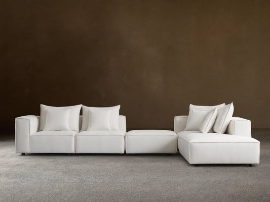 Off-white Coburn Five Piece Bumper Sectional, L-shaped, with chaise, ottoman, and 3 armless seats, on wood floor.