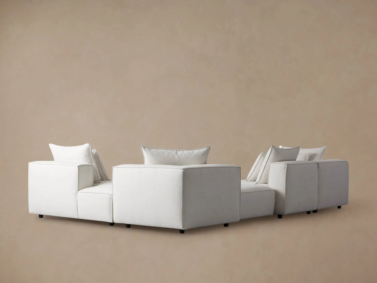 Coburn sectional: Close-up of light gray textured fabric armrest with piping, and two soft back cushions.