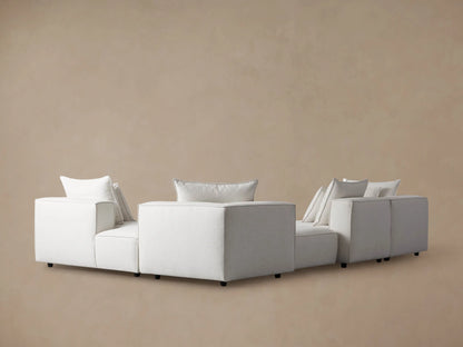 Coburn sectional: Close-up of light gray textured fabric armrest with piping, and two soft back cushions.