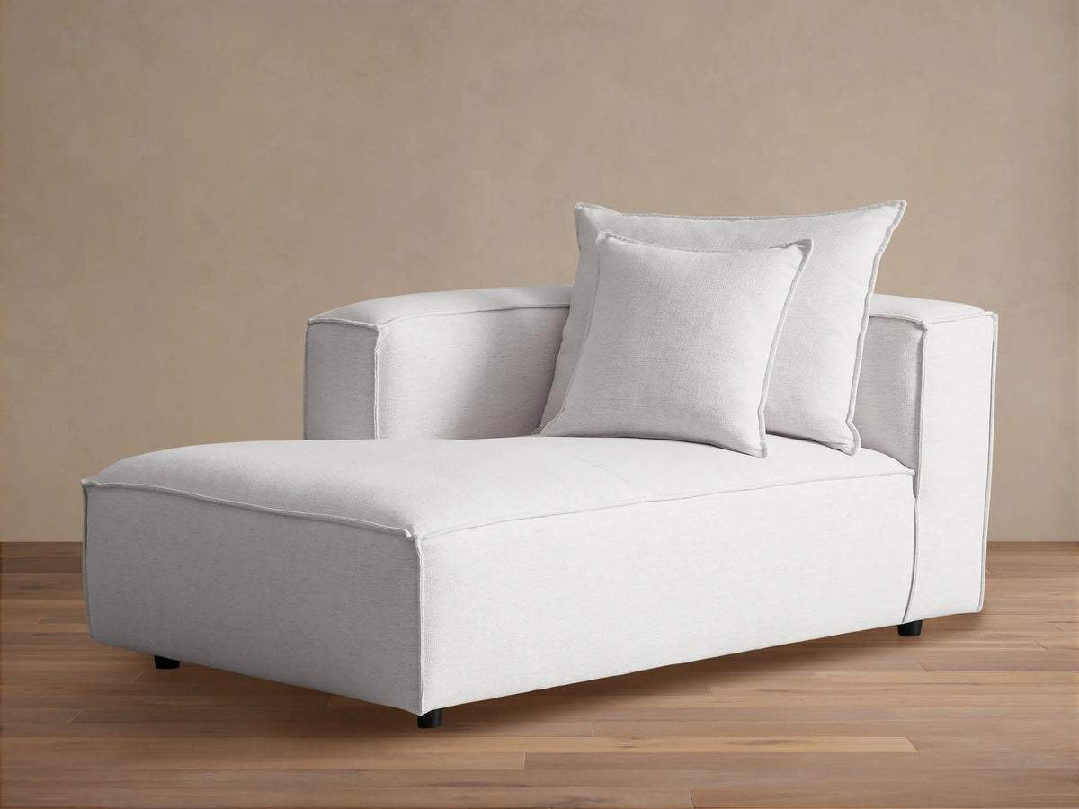 Light gray fabric Coburn Chaise, a modern lounge with two back pillows and visible stitching, sitting on a wood floor.