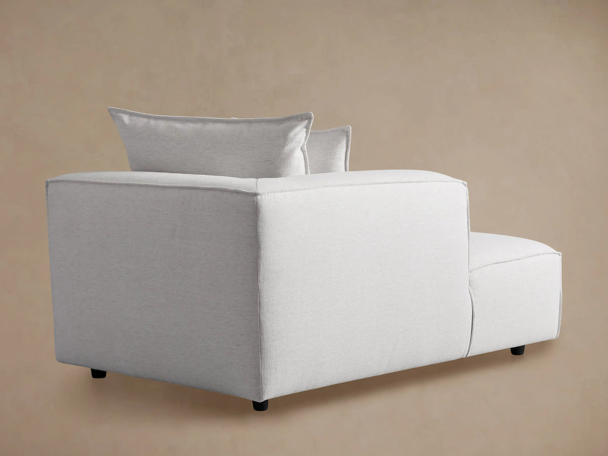 Light gray fabric Coburn Chaise, a modern lounge with two back pillows and visible stitching, sitting on a wood floor.