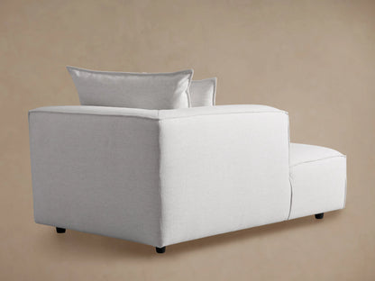 Light gray fabric Coburn Chaise, a modern lounge with two back pillows and visible stitching, sitting on a wood floor.