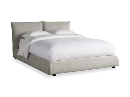 The Rigby Bed in Nomad with light gray upholstered frame, plush headboard, white bedding, and two pillows.