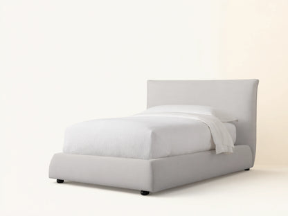 Rigby Twin Bed with light greige upholstered frame, tall headboard, and curved footboard, made up with white bedding.