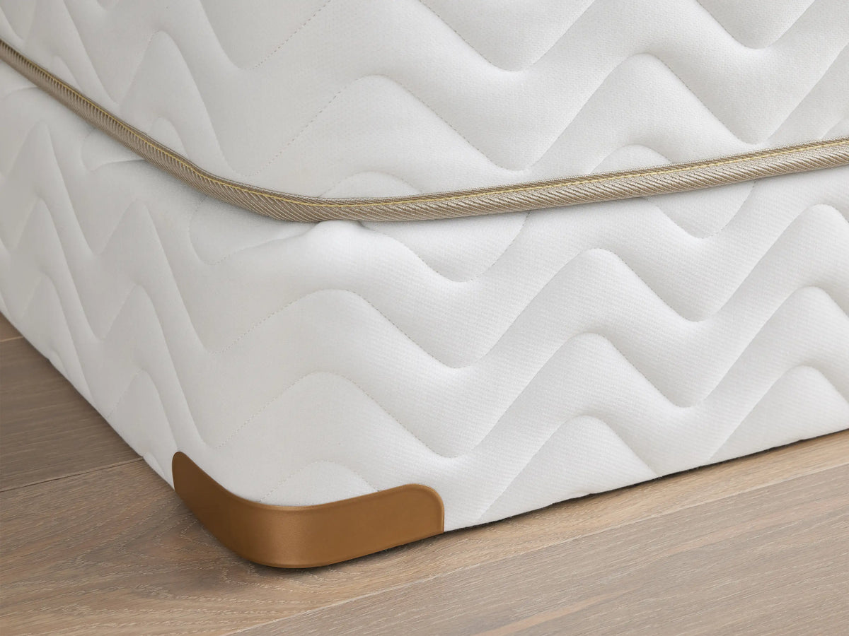 Premium Box Spring with white zigzag patterned fabric, featuring brass-finished metal corner guards on a wooden floor.