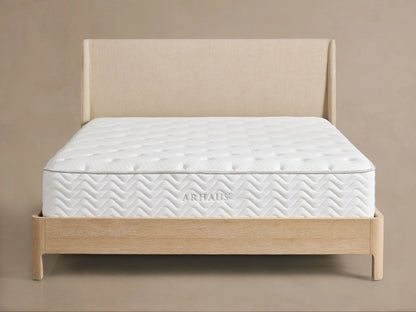 Premium firm mattress on a light wood bed frame with a beige upholstered headboard. The mattress has a quilted white surface with subtle circular patterns.