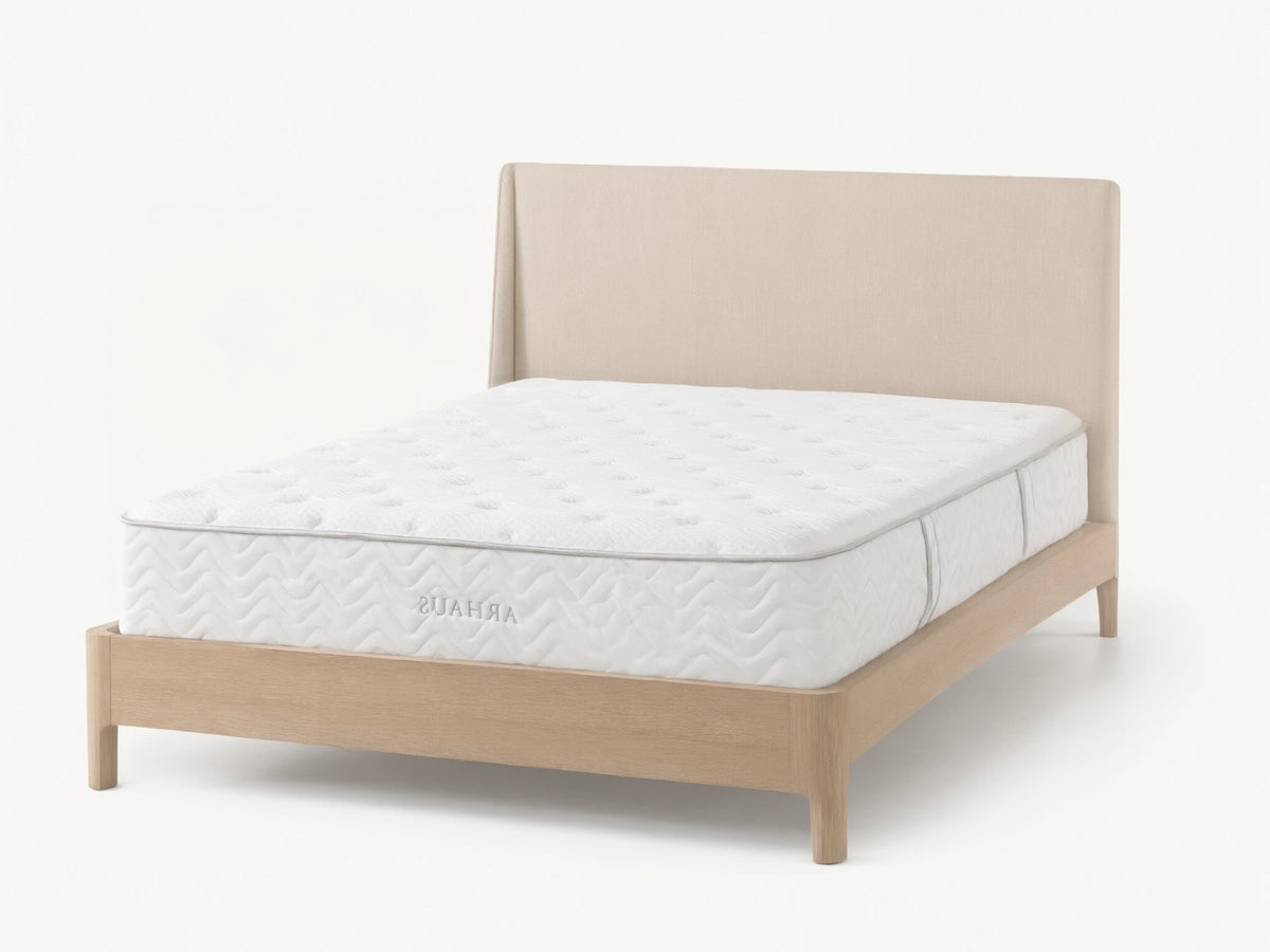 Premium firm mattress on a light wood bed frame with a beige upholstered headboard. The mattress has a quilted white surface with subtle circular patterns.