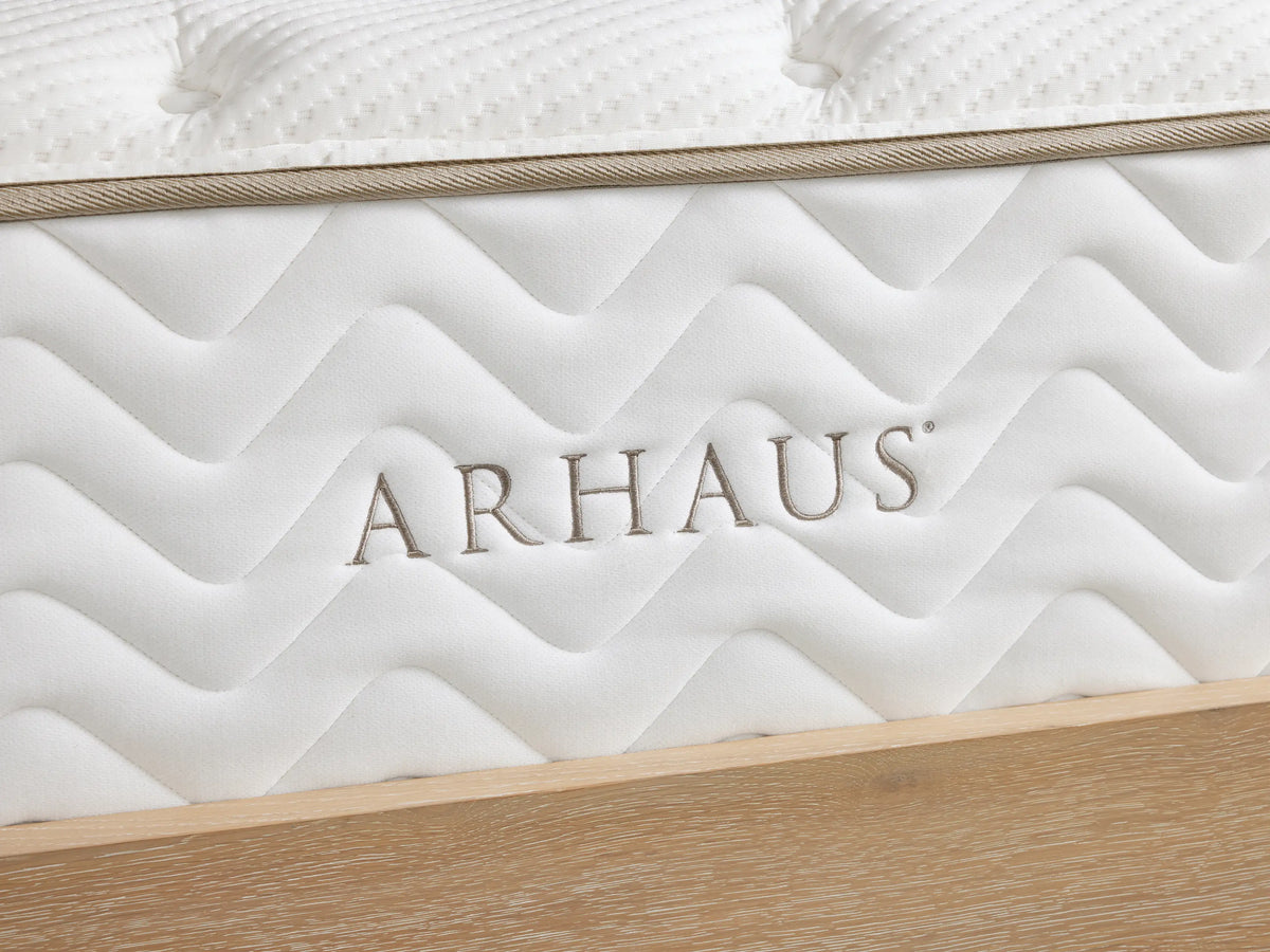 White plush mattress with quilted cotton cover, featuring tufted surface and zigzag patterned sides, resting on a wooden bed frame.