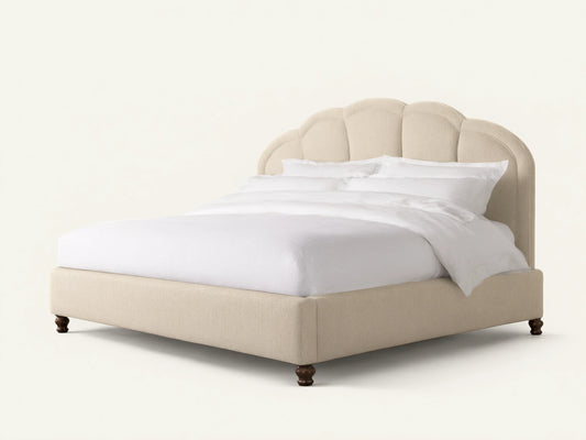 Mariel Bed with cream upholstered scalloped, channel-stitched headboard, white bedding, and dark turned legs on white background.