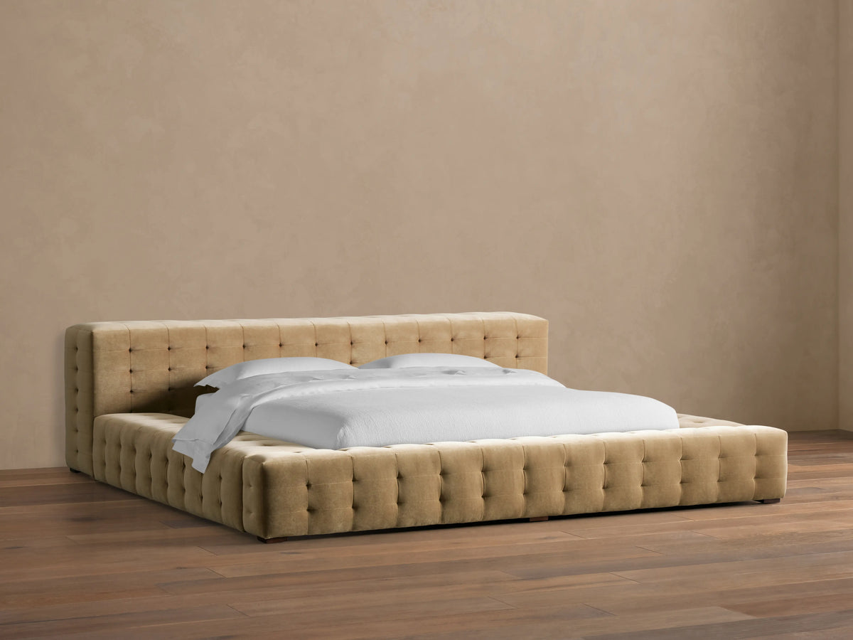 Regent Bed, light brown tufted velvet upholstery on headboard & low-profile frame with white bedding, on wood floor.