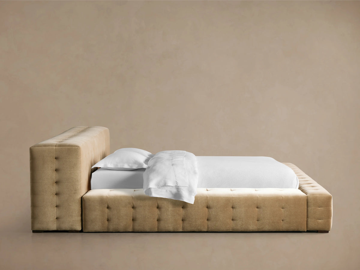 Regent Bed, light brown tufted velvet upholstery on headboard & low-profile frame with white bedding, on wood floor.
