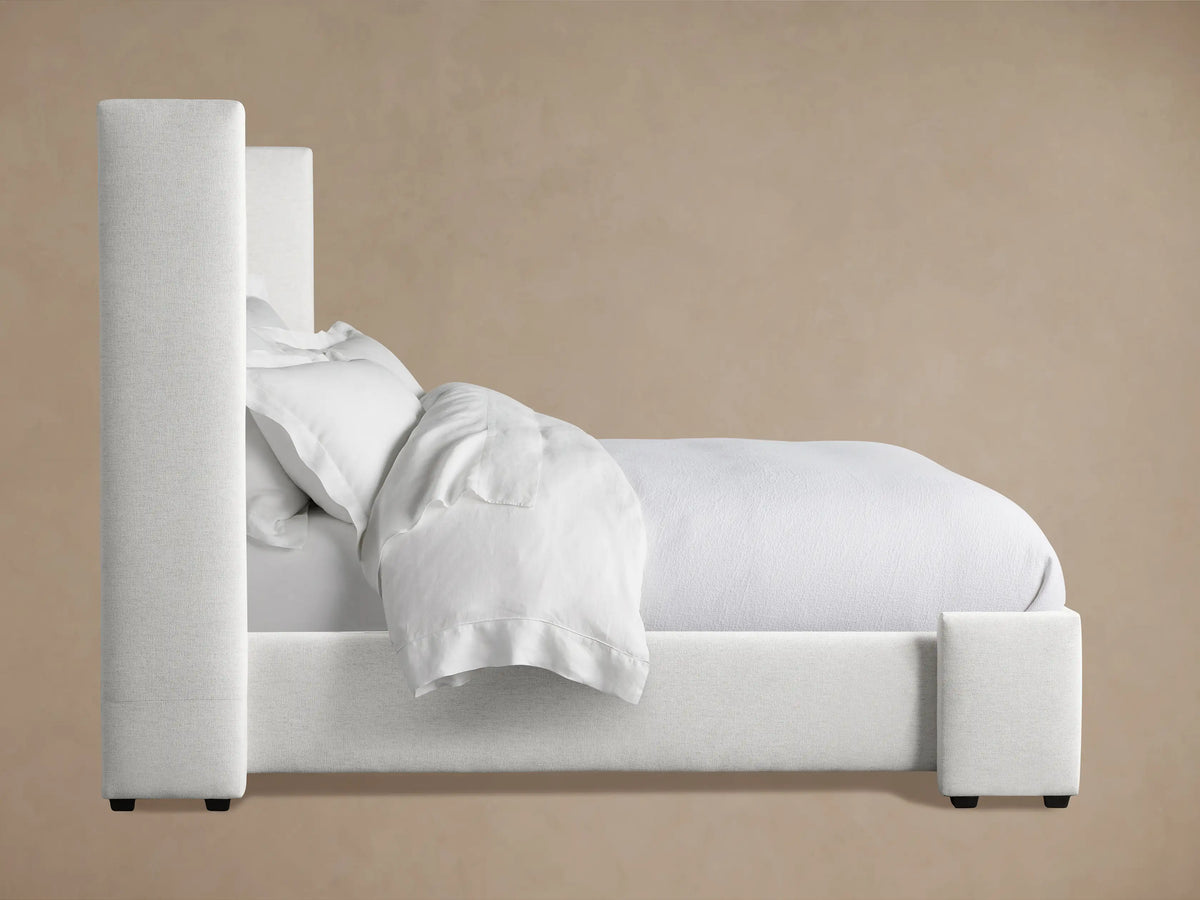 Close-up of Wyller Box-Tufted Bed headboard. Light, textured fabric shows detail of tufting and thick padded side.