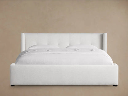 White upholstered Wyller Box-Tufted Bed with low footboard, white bedding, set on a wooden floor against beige walls.