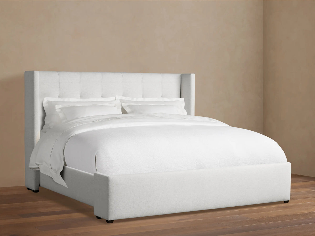 Wyller Box-Tufted Bed with low footboard. Light grey upholstered, box-tufted headboard & white bedding in an angled room.