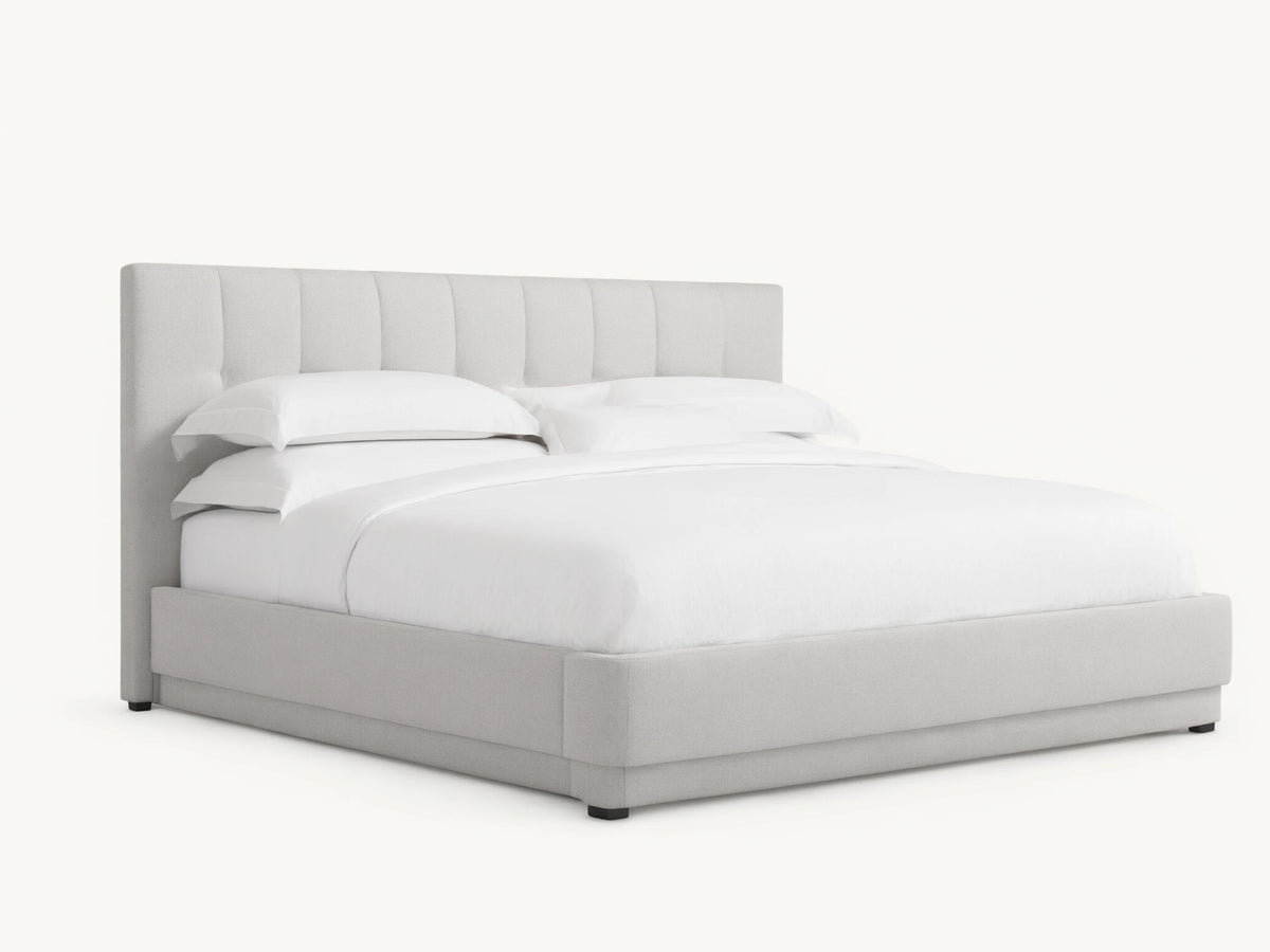 Wyller Box-Tufted Bed with low footboard. Light grey upholstered, box-tufted headboard & white bedding in an angled room.