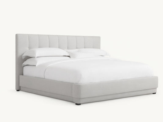Wyller Box-Tufted Bed with low footboard. Light grey upholstered, box-tufted headboard & white bedding in an angled room.