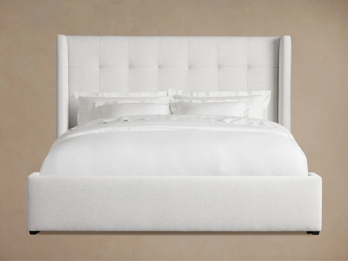 Light grey Wyller Box-Tufted Bed with low footboard & white bedding, angled in a room with brown walls and wood floor.