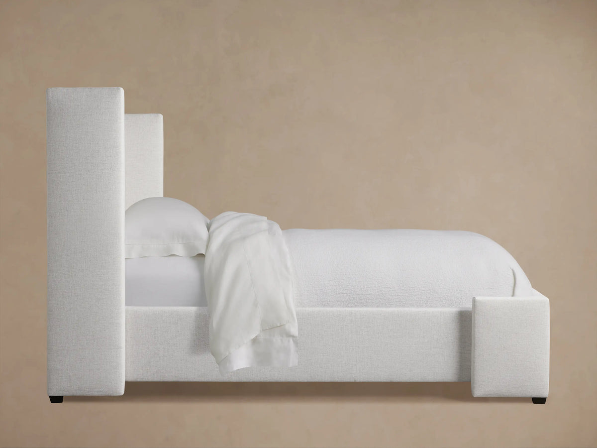 Close-up of Wyller Twin Bed headboard, showing light beige box-tufted fabric with textured upholstery & a side wing.