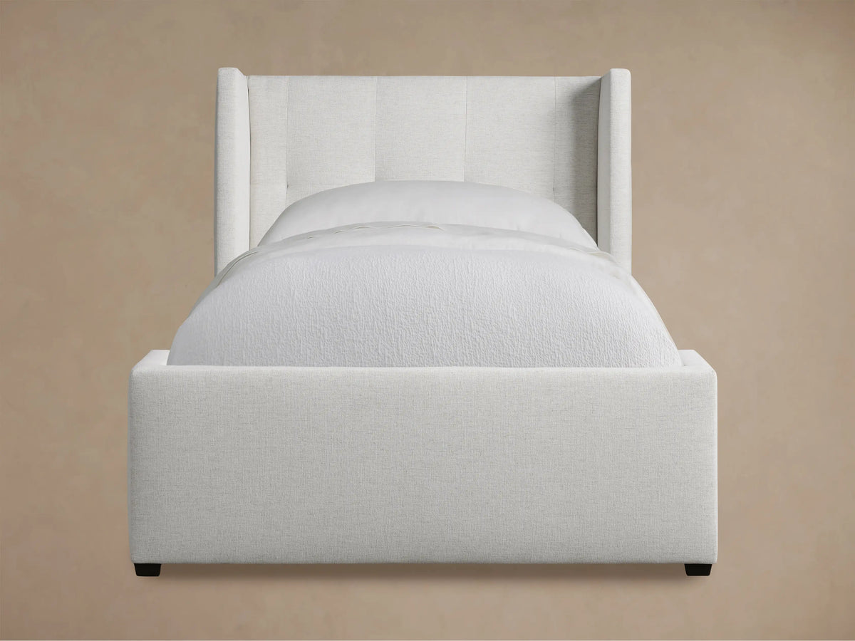 Light gray upholstered Wyller Box-Tufted Twin Bed with wingback, box-tufted headboard & white bedding on wood floor.