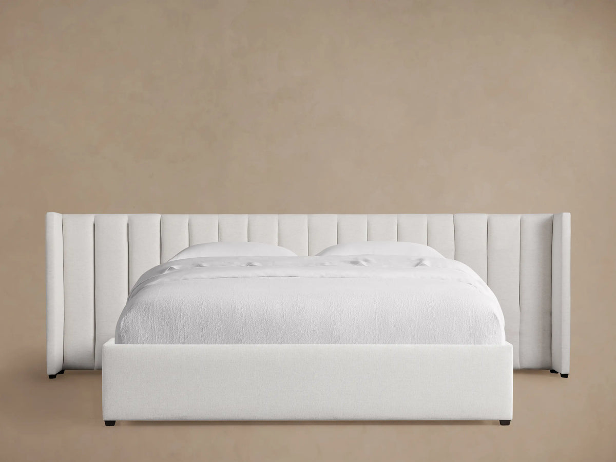 Wyller channel-stitched extended headboard bed in white, with low footboard, white bedding, on wood floor against beige wall.
