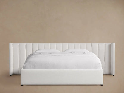 Wyller channel-stitched extended headboard bed in white, with low footboard, white bedding, on wood floor against beige wall.