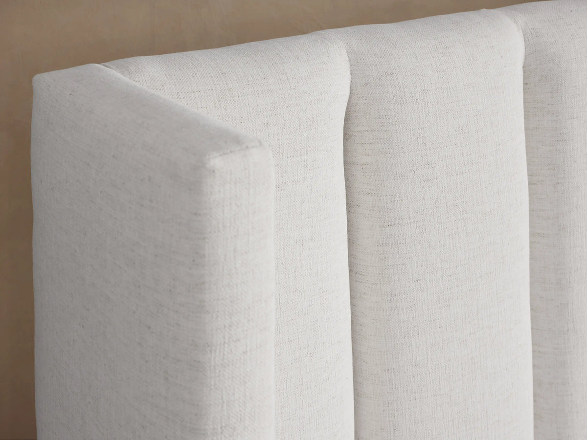 White upholstered Wyller Channel-Stitched Extended Headboard Bed with low footboard and simple white bedding.