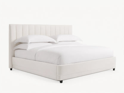 Wyller channel-stitched extended headboard bed in white, with low footboard, white bedding, on wood floor against beige wall.