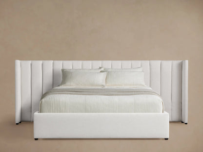 White Wyller Extended Headboard Bed with vertical channel-stitching, low footboard, white bedding, on wood floor.